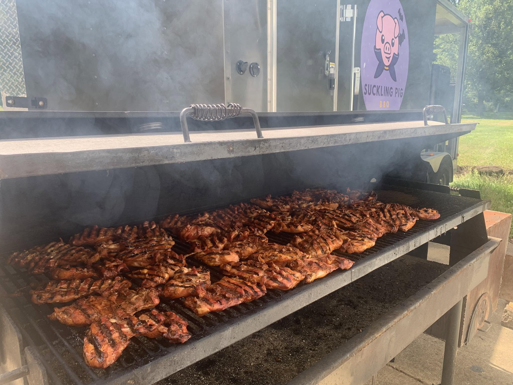 Racks of chicken and ribs smoking over live fire on the Suckling Pig BBQ pit